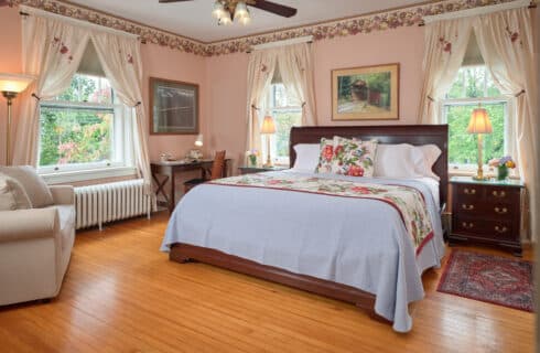 Bright guest room with queen bed in green and purple linens and two side tables with lamps