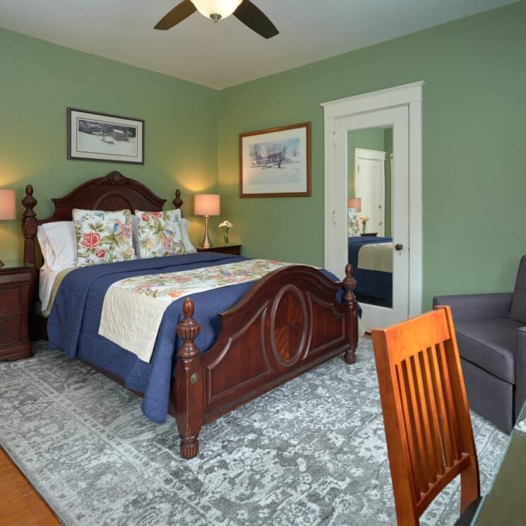 Guest room with writing desk in front of a large window, sitting chair with side table and lamp